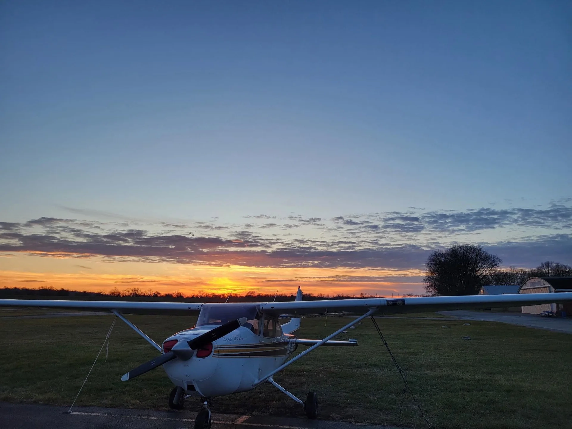 Cessna 172 tied down on the grass at sunset with a blue sky above Moraine Airpark