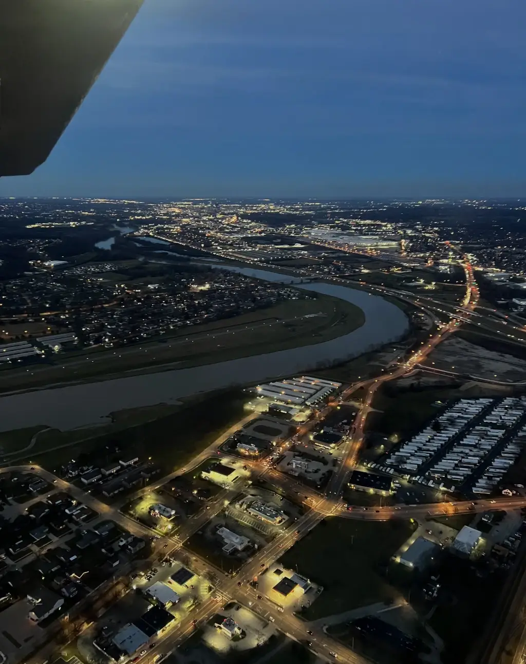 City lights and the river at dusk seen from beside the wing