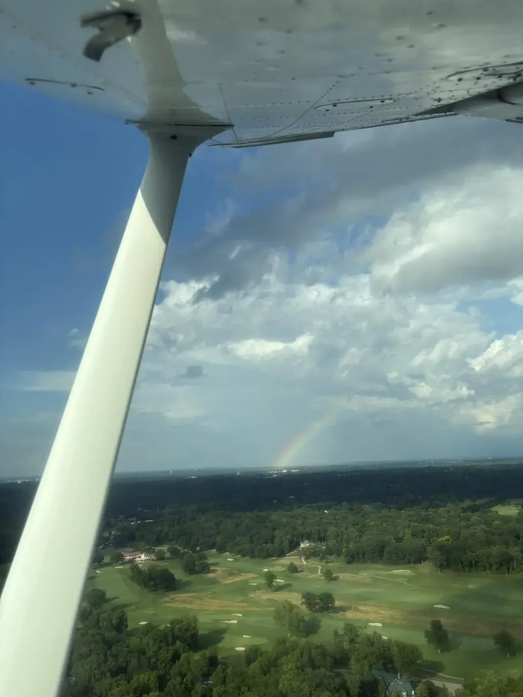 Rainbow on the horizon past the wing strut over green countryside